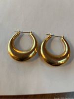 Pair of crescent-shaped gold hoop earrings on white background, front view