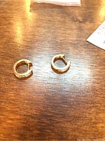 Pair of gold hoop earrings laid flat on wooden surface, front view showing diamond-set side