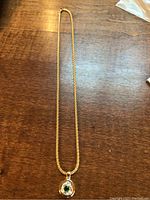 Full view of 18K yellow gold chain with emerald and diamond pendant laid on wooden surface