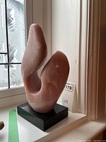 Front view of pink abstract stone sculpture on black base by window