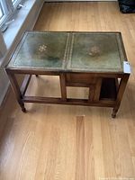 Closed table form showing green leather inlay top with gold embossed design and solid wood base with turned legs