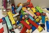 Pile of over 35 vintage PEZ dispensers with various character heads and body colors scattered in a pile