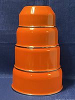 Stacked set of four orange enamel metal mixing bowls, showing nesting and size progression