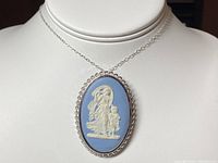 Oval Wedgwood pendant/brooch showing classical woman and child relief in white on blue jasperware background with scalloped silver frame.