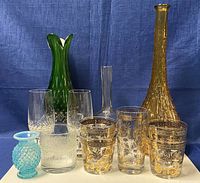 Lot showing entire collection of glassware on blue backdrop including vases, goblets, glasses, and tumbler