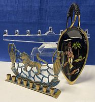 Three Judaica items grouped: clear crystal modernist menorah, brass lion menorah base, black oval painted plaque with handle
