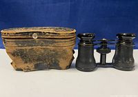 Binoculars and worn leather case side by side on white background with blue backdrop.