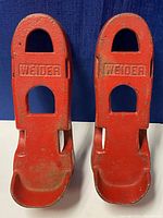 Top view of pair of red cast iron foot weights with embossed WEIDER logo, showing wear and rust spots.