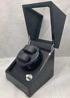 Black TRIPLE TREE watch winder with transparent hinged lid open showing two black watch pillows and control knob on front.