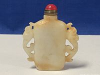 Front view showing the jade snuff bottle with carved elephant handles and red cap.