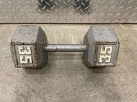 35-pound hex dumbbell showing both weight markings, metal handle, surface rust and wear. Set against a metal diamond plate background.
