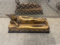 Full view of the reclining Buddha wooden statue on a decorated base showing the golden-brown finish and pose.