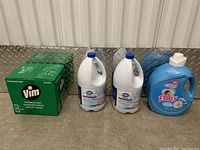Box of Vim disinfectant wipes, two 1-gallon jugs of Great Value bleach, two large blue containers of Fleecy laundry detergent.