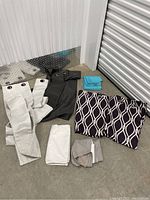 Curtains and linens laid out on the floor showing different sets including white, gray, and folded patterned purple curtains.