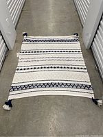 Full view of the rectangular white throw blanket with navy blue and white textured stripes and tassels in each corner.