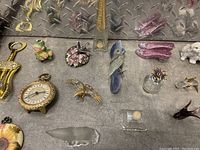 Top view of assorted glass figurines, including frog, bird, dragonfly, shoes, elephant, and other decorative pieces on gray surface with metal background.