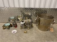 Wide shot of all household decor items arranged on the floor including turtle ashtray, elephant figurine, champagne bucket, small brass elephant, pagoda ornament, and small plate.
