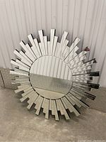 Front view of radiant sun mirror showing round mirrored center and staggered mirrored rectangular rays around perimeter.