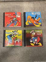 Four vintage Disney story books arranged in square on concrete floor, showing front covers and condition.