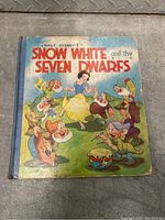Front cover of the book showing colorful illustration of Snow White dancing with the seven dwarfs with title text.