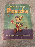 Front cover of vintage Walt Disney's Pinocchio storybook showing Pinocchio holding an apple with Jiminy Cricket beside him, some wear visible.