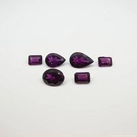 Top view of six faceted rhodolite garnet gemstones in purple color, various shapes and sizes visible.