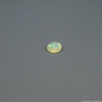 Oval faceted opal gemstone displaying color play on dark gray background