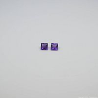 Two square cut purple amethyst gemstones side by side on a plain white background.