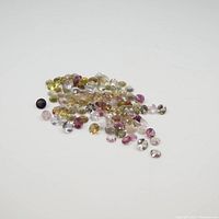 Cluster of small round mixed coloured tourmaline gemstones scattered on white surface
