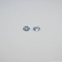 Two oval aquamarine gemstones side by side on plain background showing size and clarity