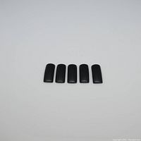 Top-down view of five (4 counted as per seller) rectangular black onyx saddle cut gemstones aligned in a row on a white background.