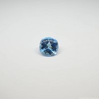 Blue topaz gemstone, cushion cut, displaying facets and clarity against white background.