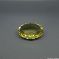 Top-angle photo of large oval lemon citrine gemstone showing clear faceted cuts and color.