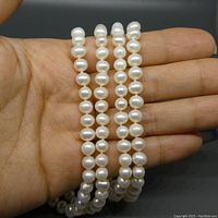 Strand of round white freshwater pearls held against a hand to illustrate size and shape.