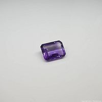 Single emerald cut purple amethyst gemstone on plain background showing cut and clarity.