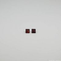 Two square garnet gemstones placed on a white background showing their color and cut clearly.
