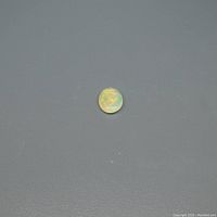Close-up photo of an oval cabochon opal gemstone displaying a white/yellow base with multicolor flashes, lying on a dark flat surface.