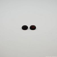 Two oval-shaped garnet gemstones with concave cuts and deep red color on a white background.
