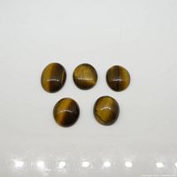 Top-down view of five oval cabochon tiger eye gemstones placed on a white surface, showing the color and chatoyancy.