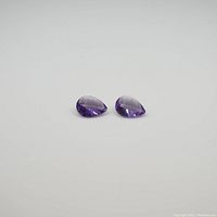 Two pear-shaped purple amethyst gemstones on a white background showing clarity and color.
