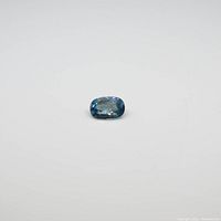 Close-up photo of a single oval blue zircon gemstone on white background, showing its faceted cut and color.