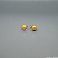 Front view of the pair of cream/yellow round pearl stud earrings on a grey background showing shape and color.