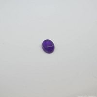Oval cabochon cut purple amethyst gemstone shown from wide angle on white background.
