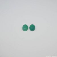 Top-down view of two small oval green chalcedony cabochon gemstones on white background.