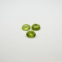Three oval yellow-green peridot gemstones displayed on a white background, clearly showing their faceted cut and color.