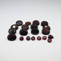 Overview of twenty natural garnet gemstones arranged in rows, showing various sizes and mixed round, pear, and oval shapes with rich red color.