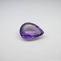 Pear shaped purple amethyst gemstone shown from an angle highlighting facets and color.