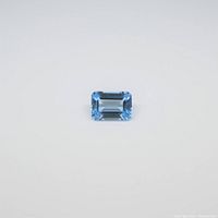 Front view of the rectangular emerald cut blue topaz gemstone on white background, showing facets and color.