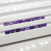 Eighteen emerald cut amethyst gemstones displayed in two rows showing the range of purple shades and emerald cut shape.