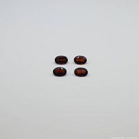 Four oval-shaped dark red garnet gemstones placed on white surface, showing size and color of stones clearly.